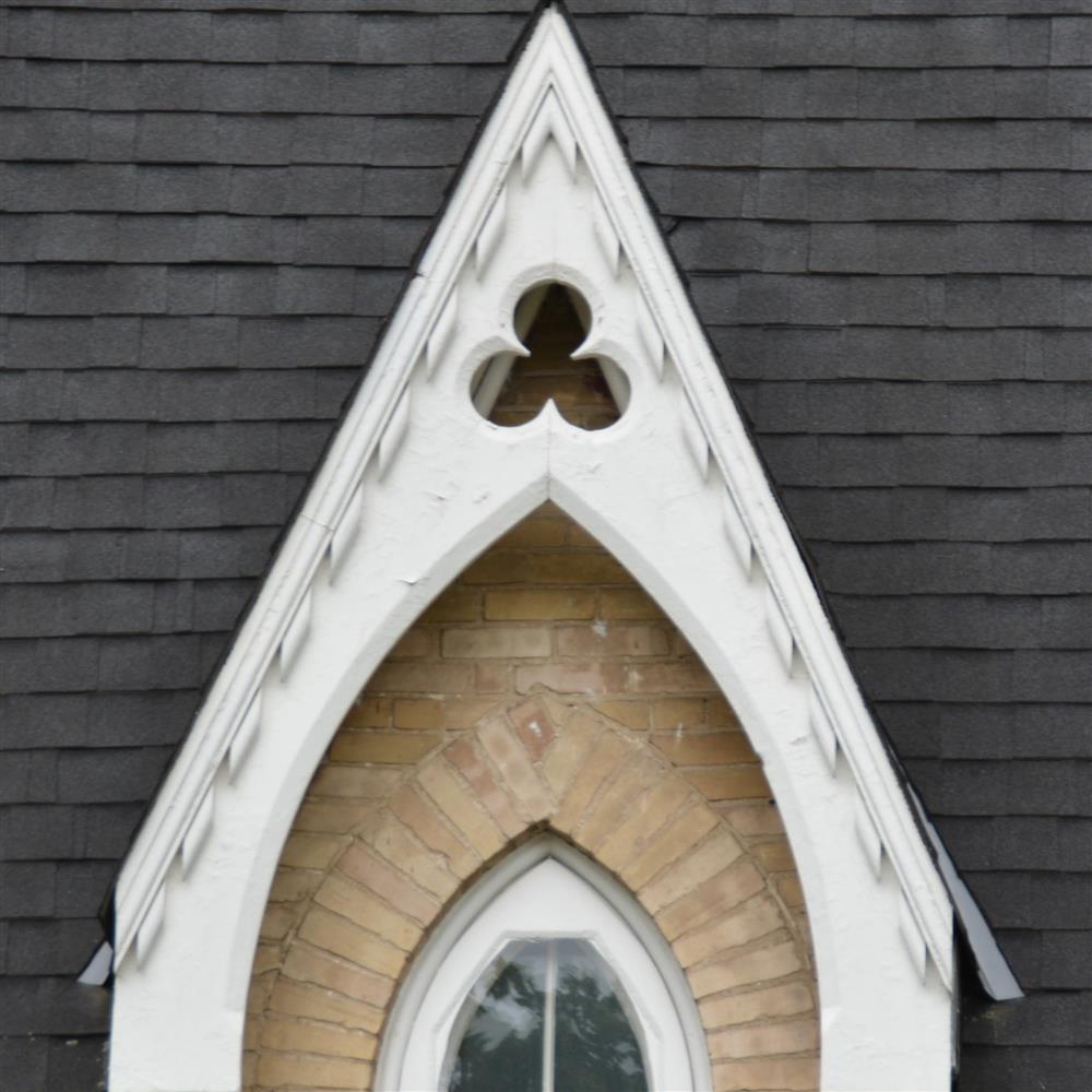 Trim over a window forms a sharp triangle with a clover cut-out detail, wood painted white